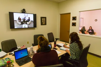 Two learners at a table looking a TV doing work