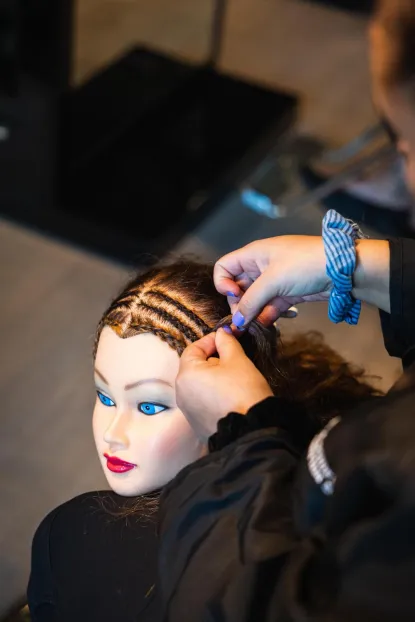 hands braiding hair on a practice mannequin
