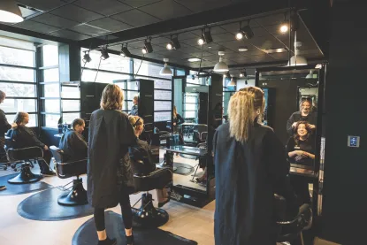 Multiple people in light filled, hair salon with black furnishings