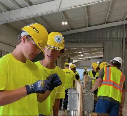 Students in yellow shirts and hard hats working on electrical project