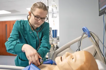 Young woman nursing student using stethoscope on training manikin in nursing lab