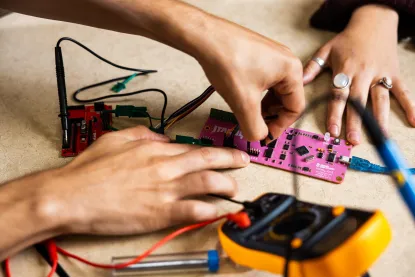Hand working on brightly colored circuit board and portable electrical device
