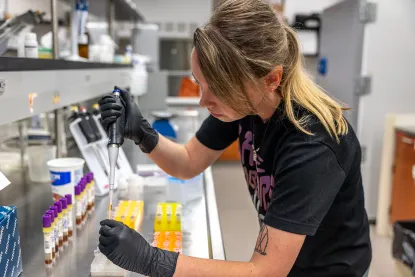 Young woman with syringe putting samples in test tubes in biology lab