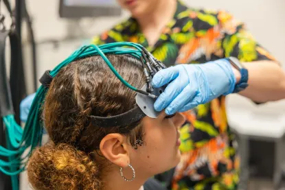 Young woman having Functional Near-Infrared Spectroscopy (fNIRS) device placed on her head in psychology lab