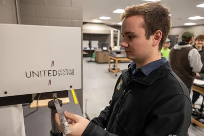 Young man using United Testing Machine to exert pressure on strip of metal 