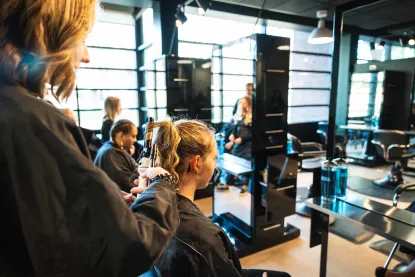 Students working on clients' hair in light-filled cosmetology classroom