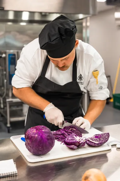 Male student chef carefully slices red cabbage for recipe preparation
