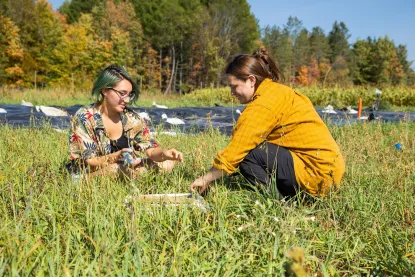 Two young women in an outdoor field collecting seed samples