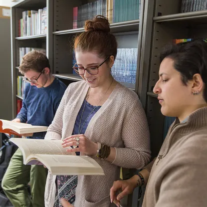 Students looking at a book against a bookshelf