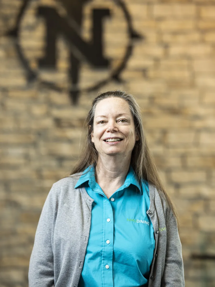 Laurie Schneider standing in front of brick wall with NMU's torch logo.