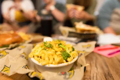 Mac & Cheese on the table with food and people in the background