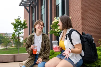 Two students sitting outside of Jamrich talking with beverages in their hands.