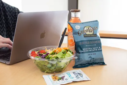 A salad and chips sitting next to a Macbook on a table in Jamrich