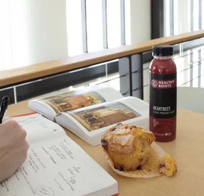 A partially eaten muffin, drink, and open textbook on the table where a student is taking notes in Jamrich