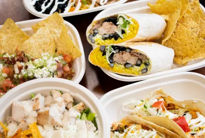 A variety of Fieras food including burritos, tacos, salads, and guac sitting on a wooden table.