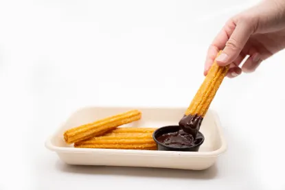 A hand dipping a churro into chocolate sauce.