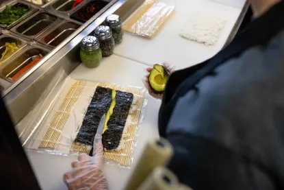 avocado being placed onto nori to make a sushi roll