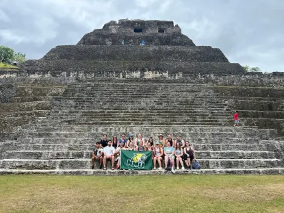 Students holding an NMU flag in front of ancient ruins in Belize