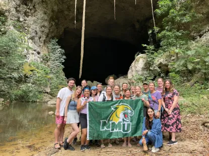 Students in Belize in front of a cave holding an NMU Wildcat flat