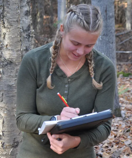Photo of student taking field notes in Dead River Community Forest