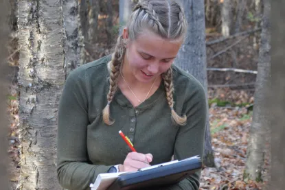 Student taking field notes in the Dead River Community Forest.