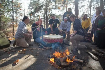 students sitting around a fire with a Native American drum