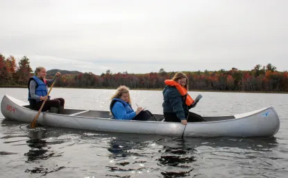 Three students in a silver canoe practicing hydrology measurements.