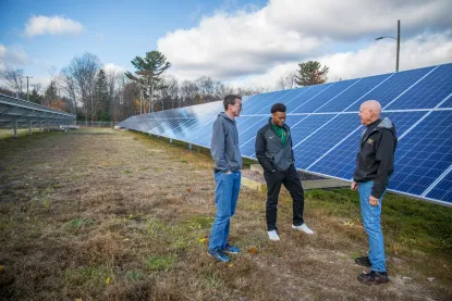 two male students talking to a male instructor while standing next to a large solar panel