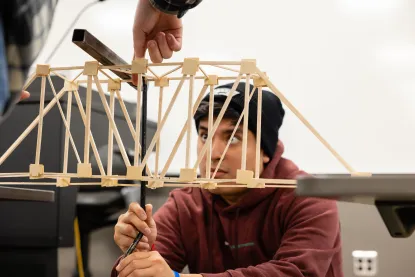 Student testing the strength of his balsa wood bridge