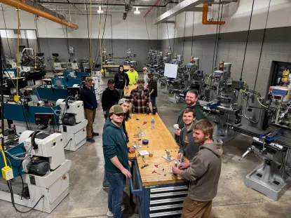 A groups of students standing around a table in the CNC lab working on a lab project.