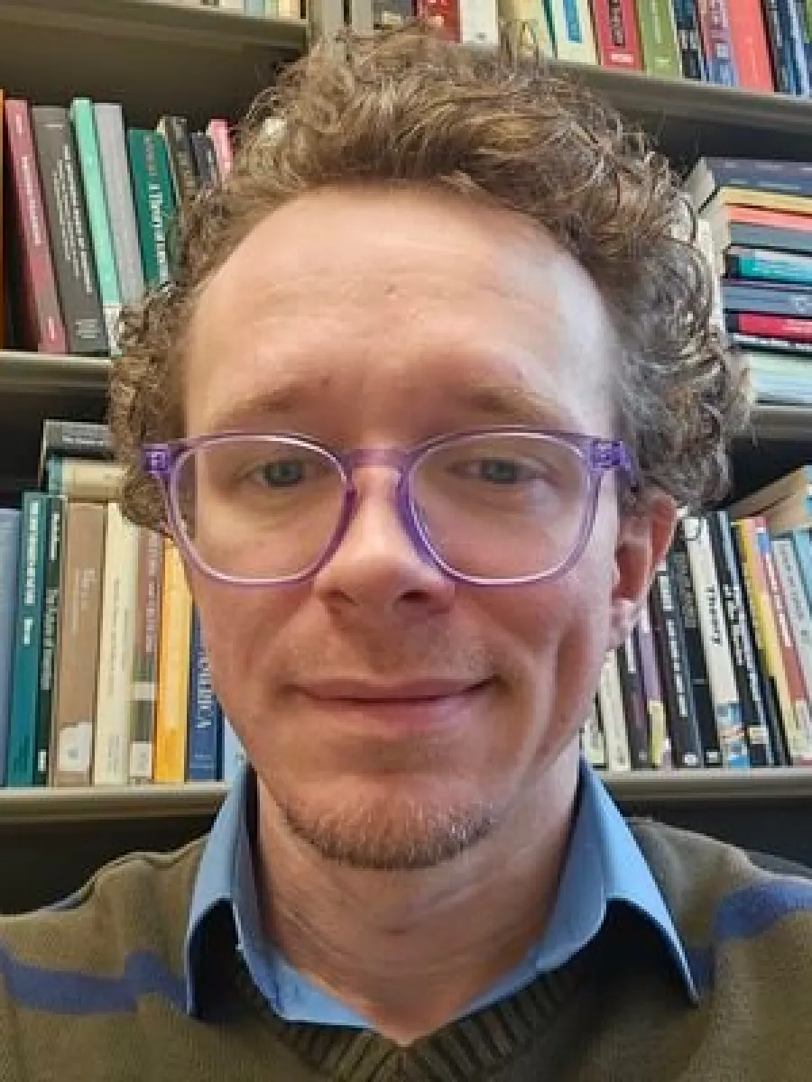 Portrait photo of Ben Wetherbee with a bookshelf behind him