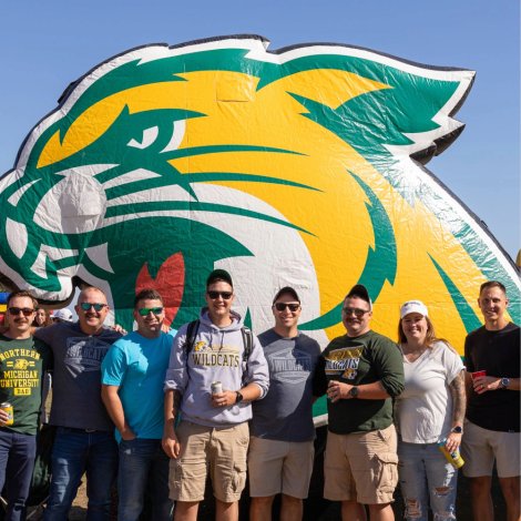 Group of people standing outside in front of the NMU cat head, dressed in green and gold 
