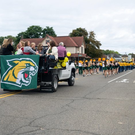 Street with parade floats, including a marching band and people watching from the side of the street.