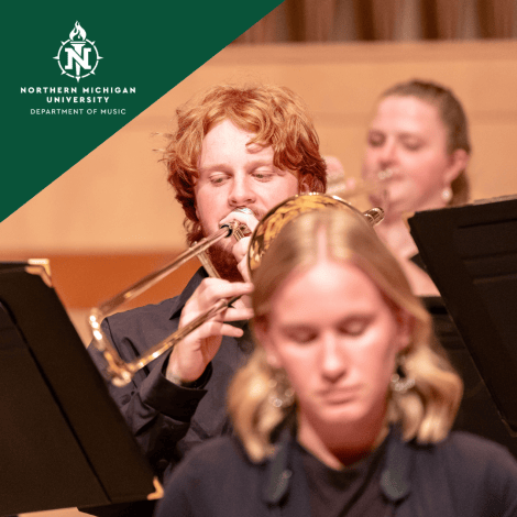 Northern Michigan University music students play brass instruments, with a focused trombonist in sharp focus behind a blurred classmate; warm, collaborative concert-hall atmosphere.