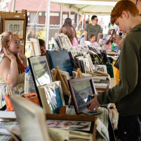 Student shopping in an art fair looking at a booth with paintings 