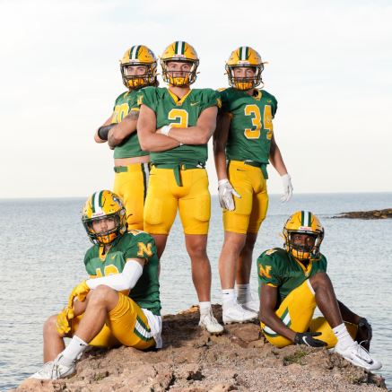 three football players standing and two sitting on a rock near the shore of Lake Superior