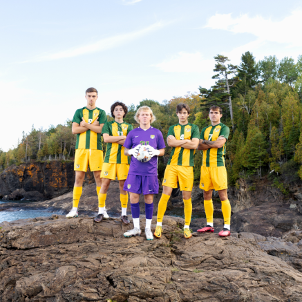 five male soccer players standing on the shore of lake superior