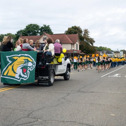 Street with parade floats, including a marching band and people watching from the side of the street.