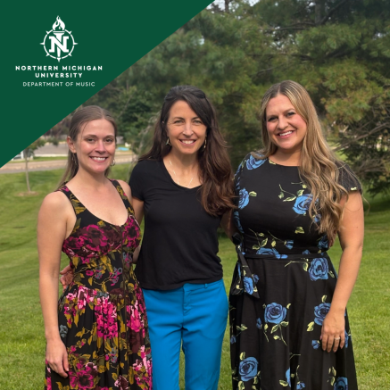Three smiling women pose outdoors on a lawn, wearing colorful dresses and bright pants, beneath the Northern Michigan University Music logo.