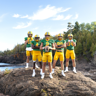 five football players standing on a rock on the the shore of Lake Superior