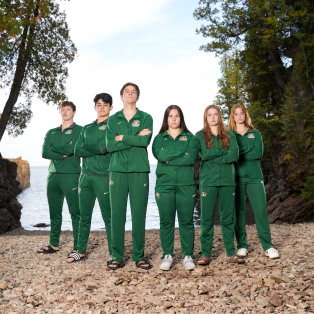 three male swimmers and three female swimmers standing on the shore of Lake Superior