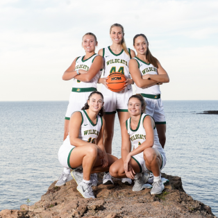 five women basketball players standing on a rock on the shore of Lake Superior