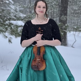 Jaymes in an emerald green skirt and black top, holding her violin in the snow