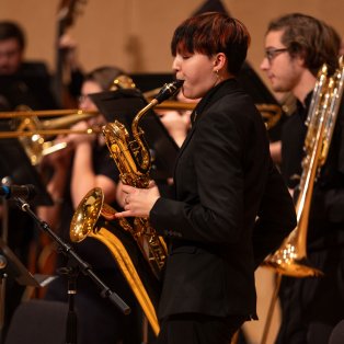 NMU student wearing an all black suit standing holding and playing a tenor saxophone