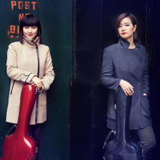 Beijing Guitar Duo Standing next to each other, one in a tan coat with a red case and one in a long, black coat with a black case