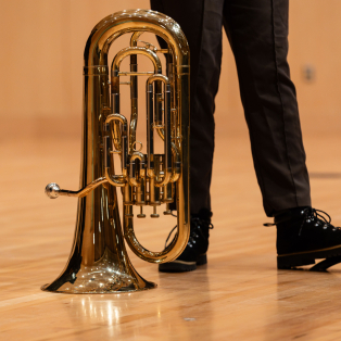 A baritone sits bell-down on the stage, next to a student with black pants and black shoes