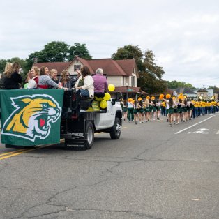 Street with parade floats, including a marching band and people watching from the side of the street.