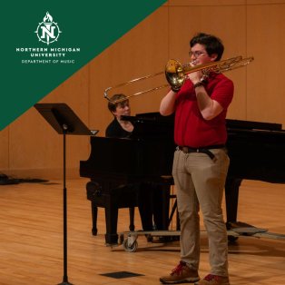 Northern Michigan University music performance: a trombonist in red plays onstage while a pianist accompanies him at a grand piano.