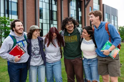 A group of students link arms in front of the Jamrich academic building on NMU's campus