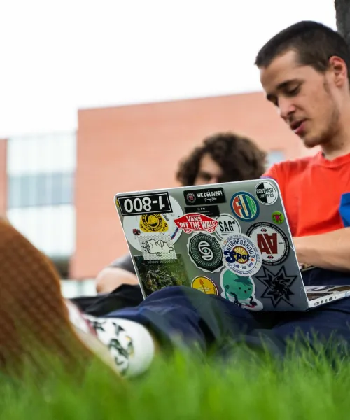 Male student on laptop sitting on ground by a tree